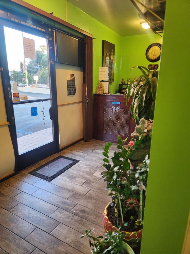 The entry hall looking back at the glass front door, with a doormat, potted plants and the corner of the wooden front desk.